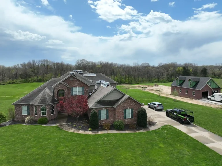 Aerial view of a residential property in Wentzville with a well-maintained lawn and a roof under repair. Vehicles are parked in the driveway.