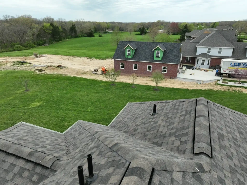 An aerial view of a residential area showing rooftops with new shingles and a construction site in the background, indicating storm damage roof repair in Wentzville.