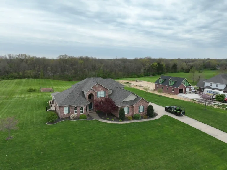 Aerial view of a spacious house in Wentzville, surrounded by a lush green lawn and trees, with a driveway leading to the garage.